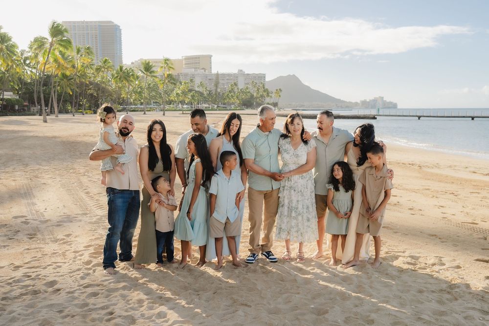 Large family posing together on a sandy Hawaiian beach with Diamond Head crater and palm trees in the background.