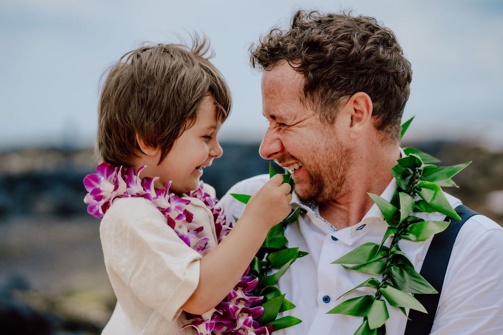 A couple shares joyful laughter while wearing traditional Hawaiian leis during a sunset photo session.