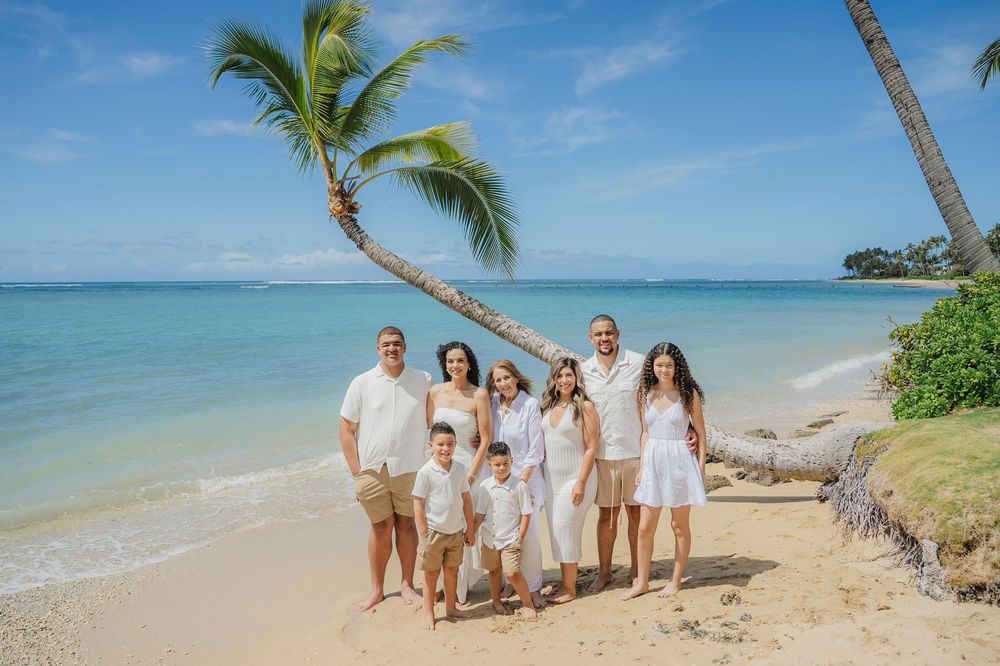 A group in white outfits walks along a scenic tropical beach with palm trees and turquoise water on a sunny day.
