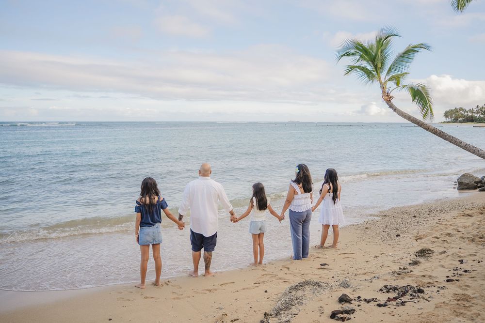 A group of people walking along a tropical beach with palm trees and turquoise water in the background.