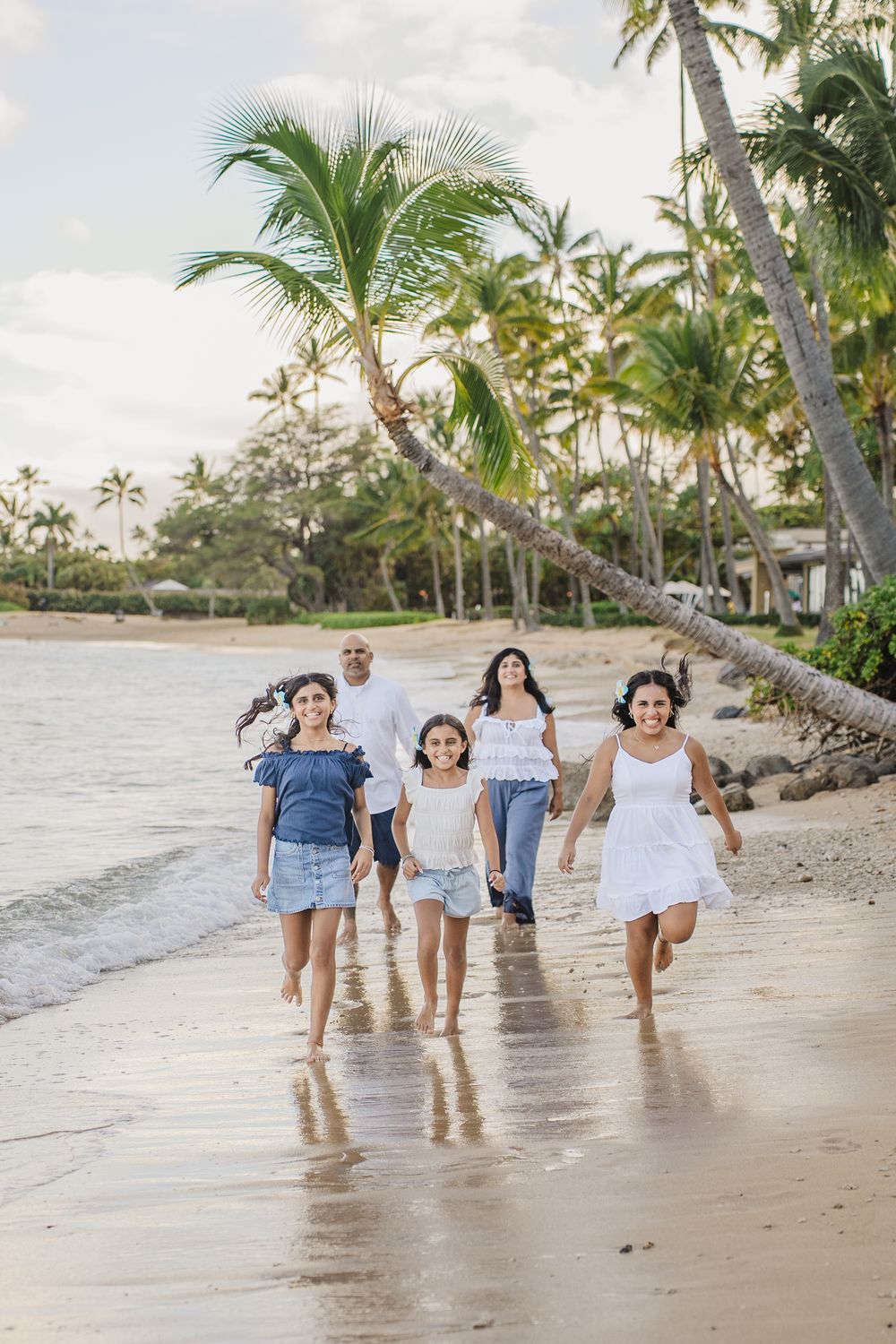 Group of friends walking together along a tropical beach shoreline with palm trees in Hawaii at sunset.
