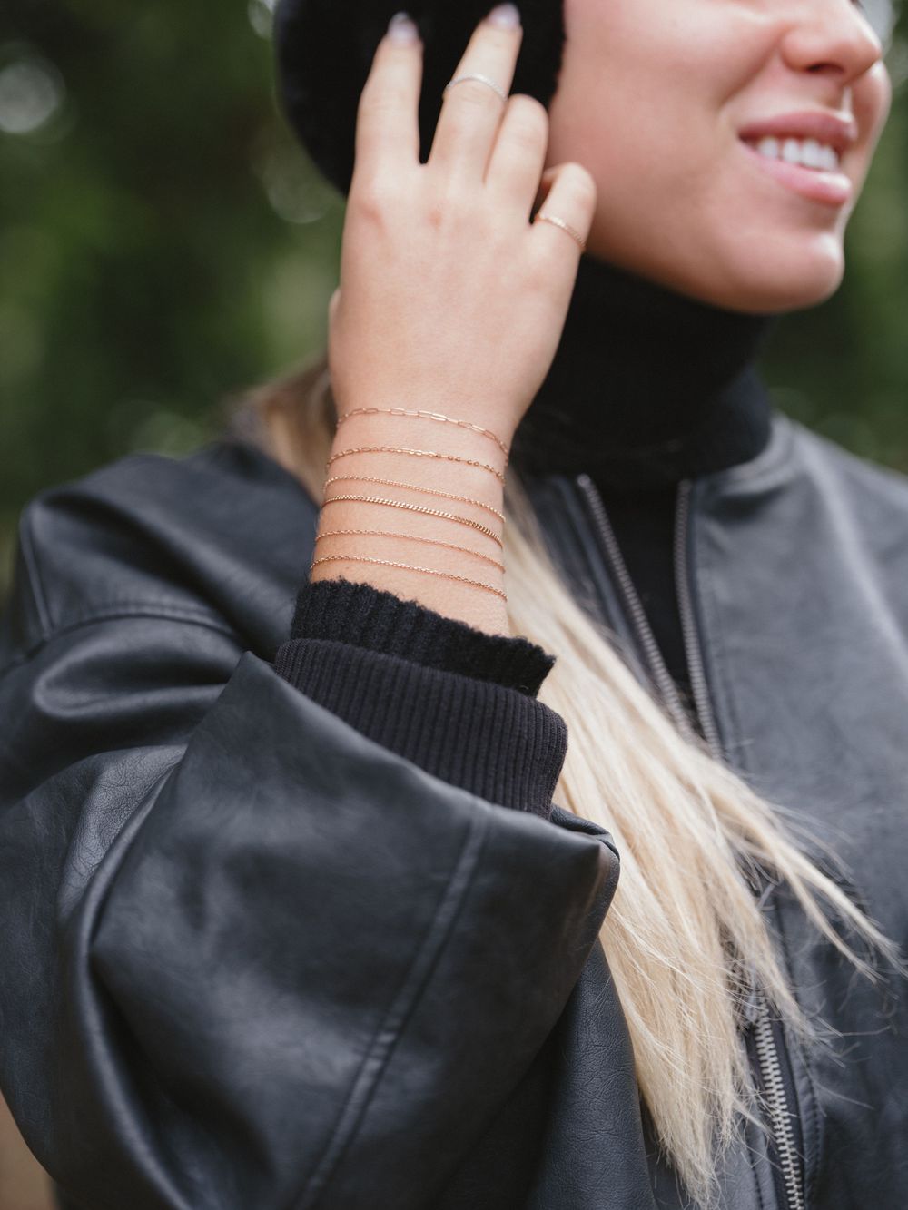 Delicate rose gold chain bracelets layered on wrist with black turtleneck visible.