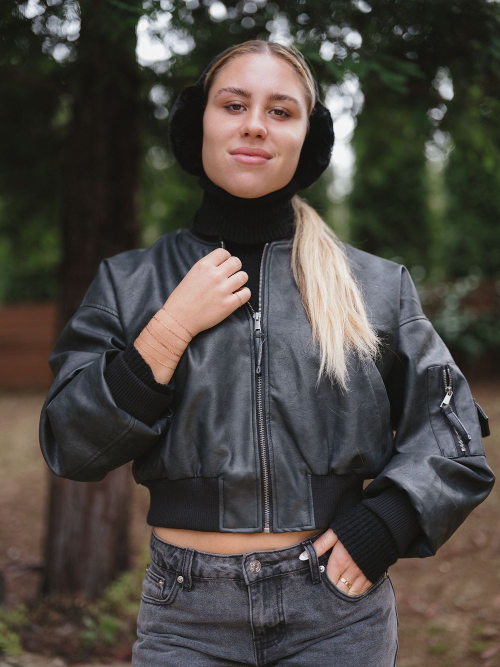 Stylish black bomber jacket paired with denim and black headwear in outdoor setting.