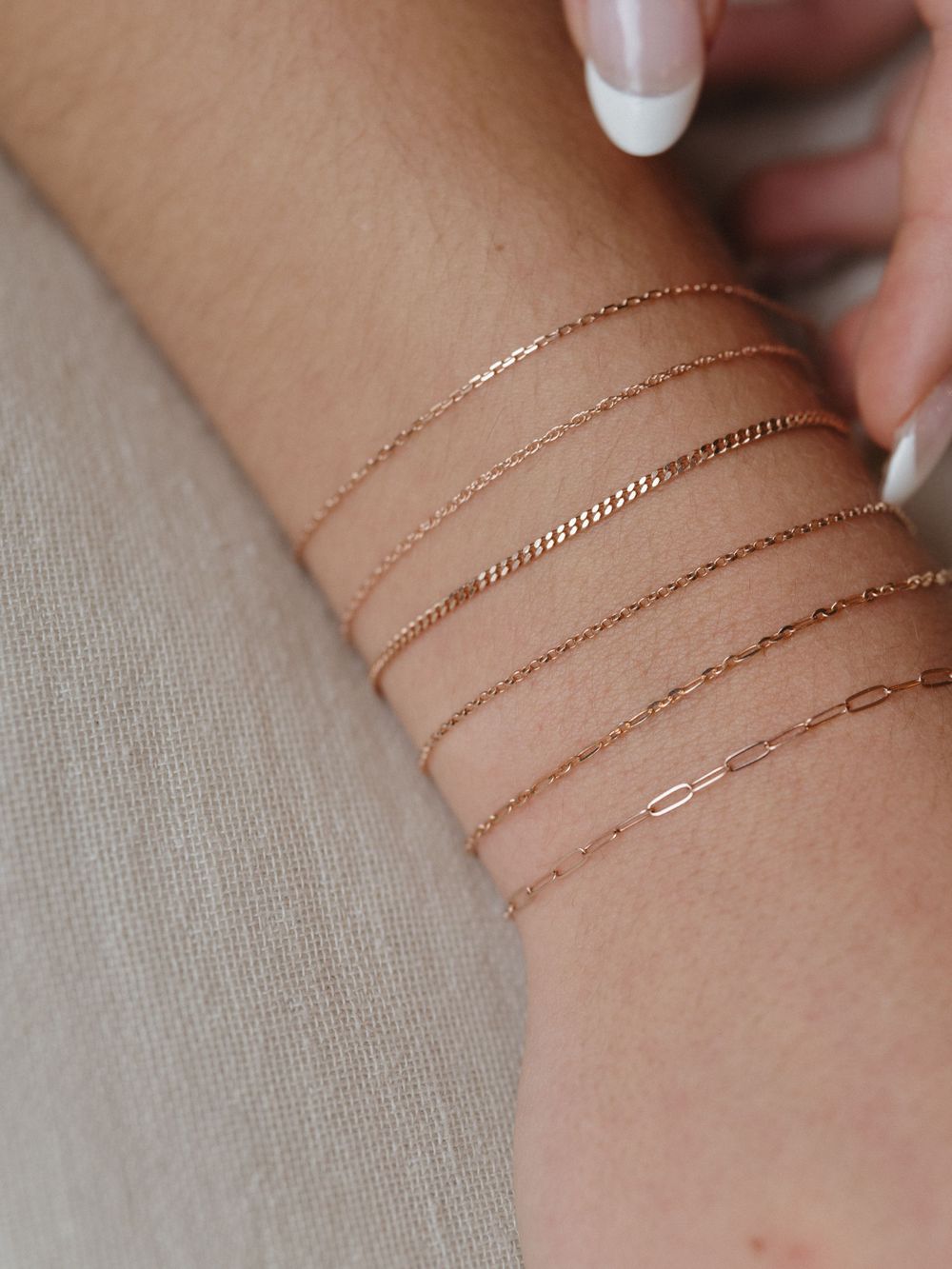 Multiple fine rose gold chain bracelets layered on wrist with french manicured nails.