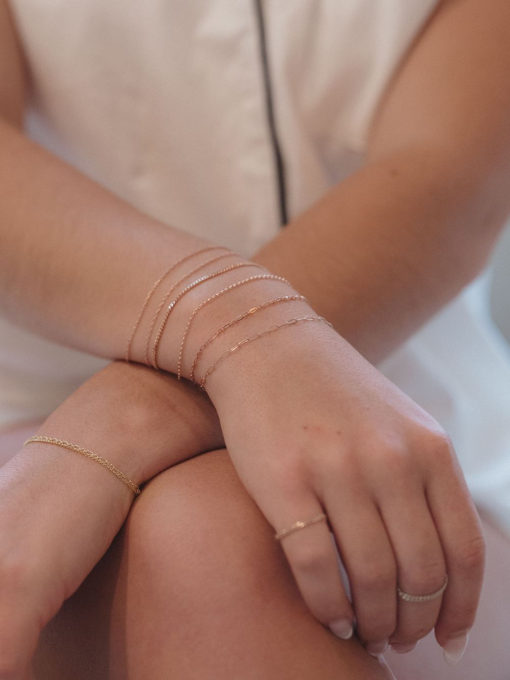 Delicate layered gold bracelets adorning a wrist with dainty rings on fingers.