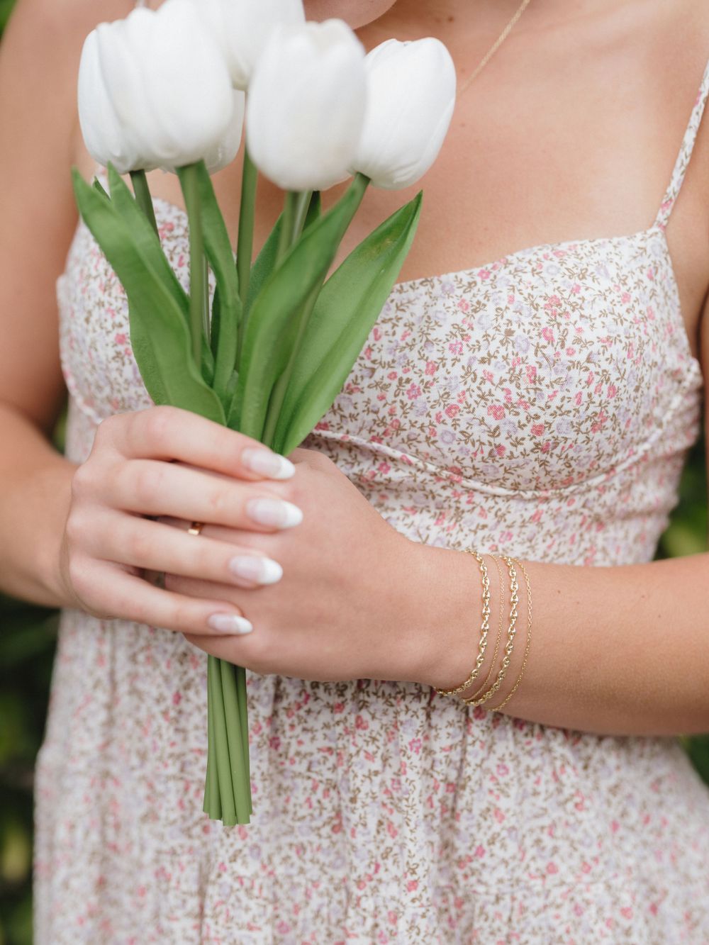 Hands holding white tulips against a floral print dress with dainty gold bracelet details.
