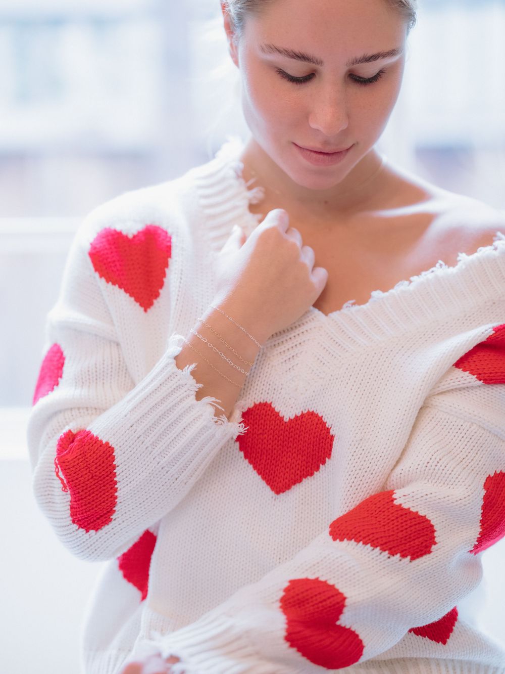 Cozy white knit sweater decorated with red heart patterns throughout.