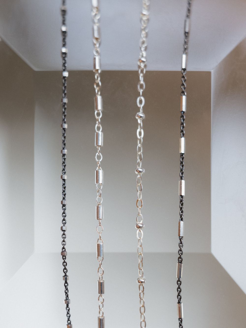 Four different styles of silver chain necklaces hanging vertically against a white background.