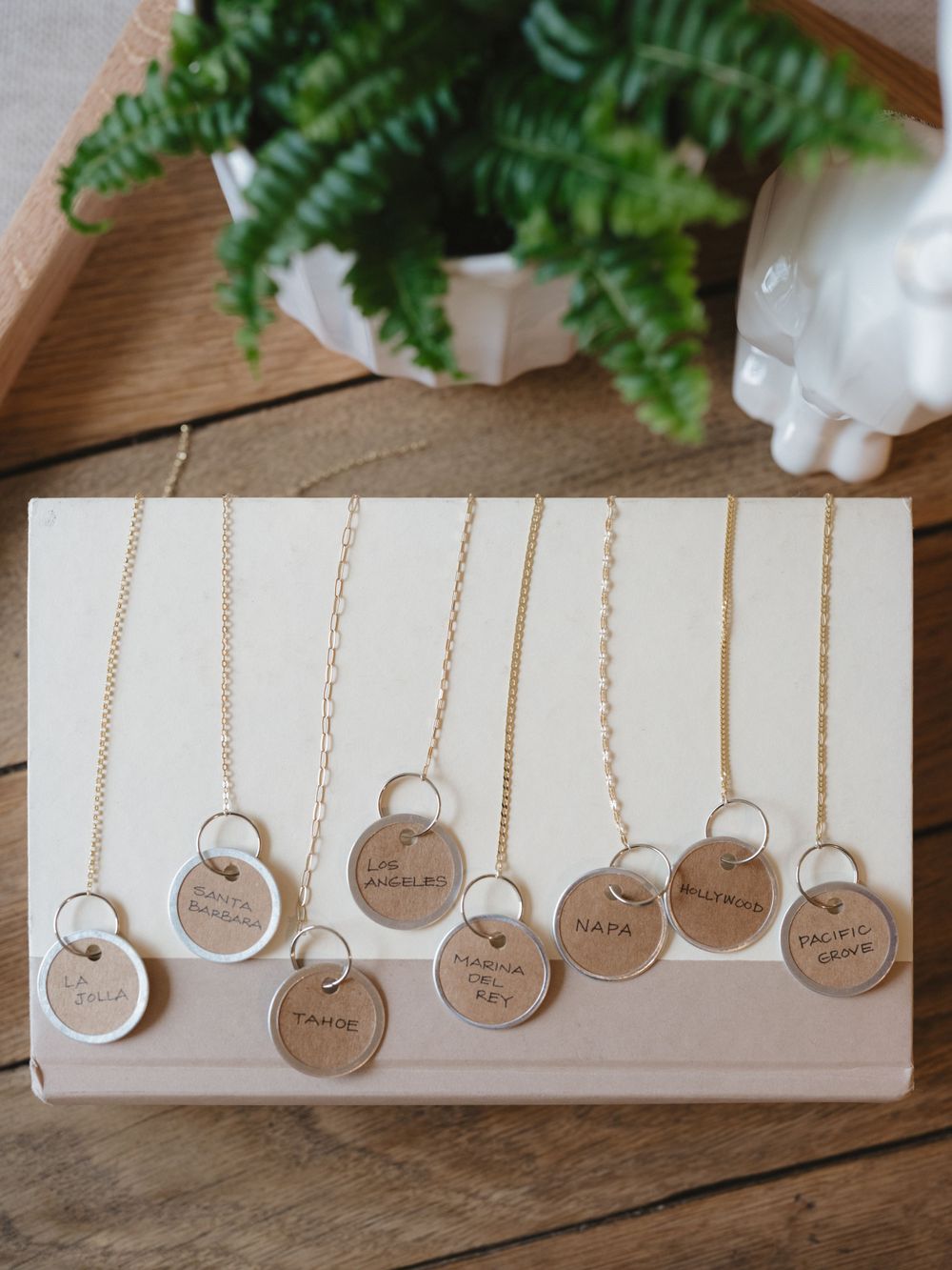 Display of multiple dainty gold necklaces with round pendant charms laid on wooden surface.