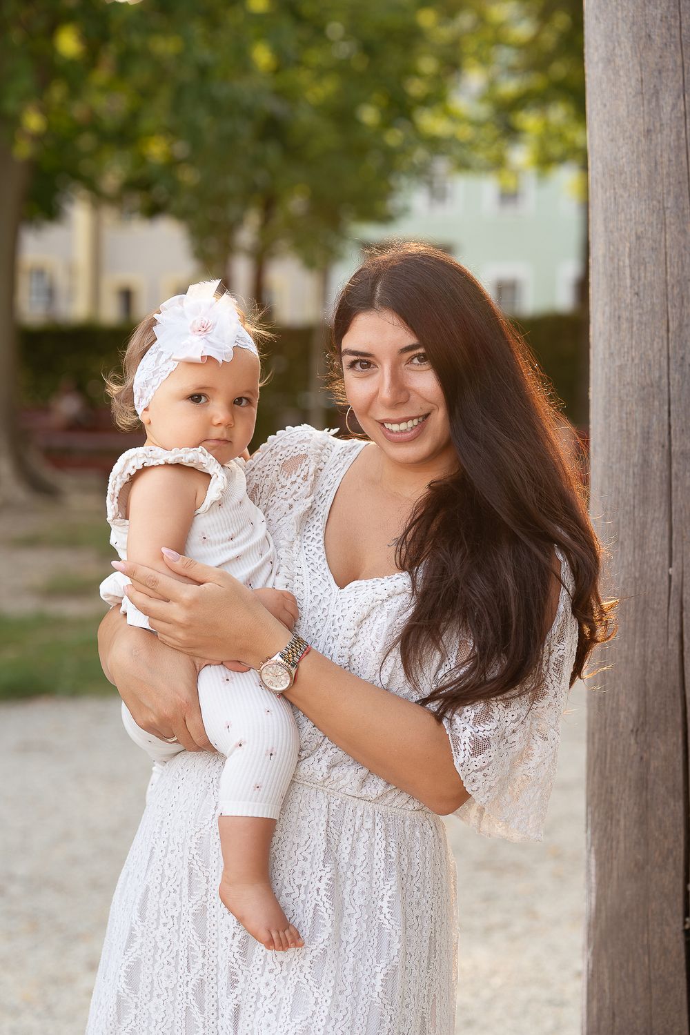 Familienfotografie - A sweet outdoor portrait of a baby and a mother in matching white outfits against a natural garden backdrop.