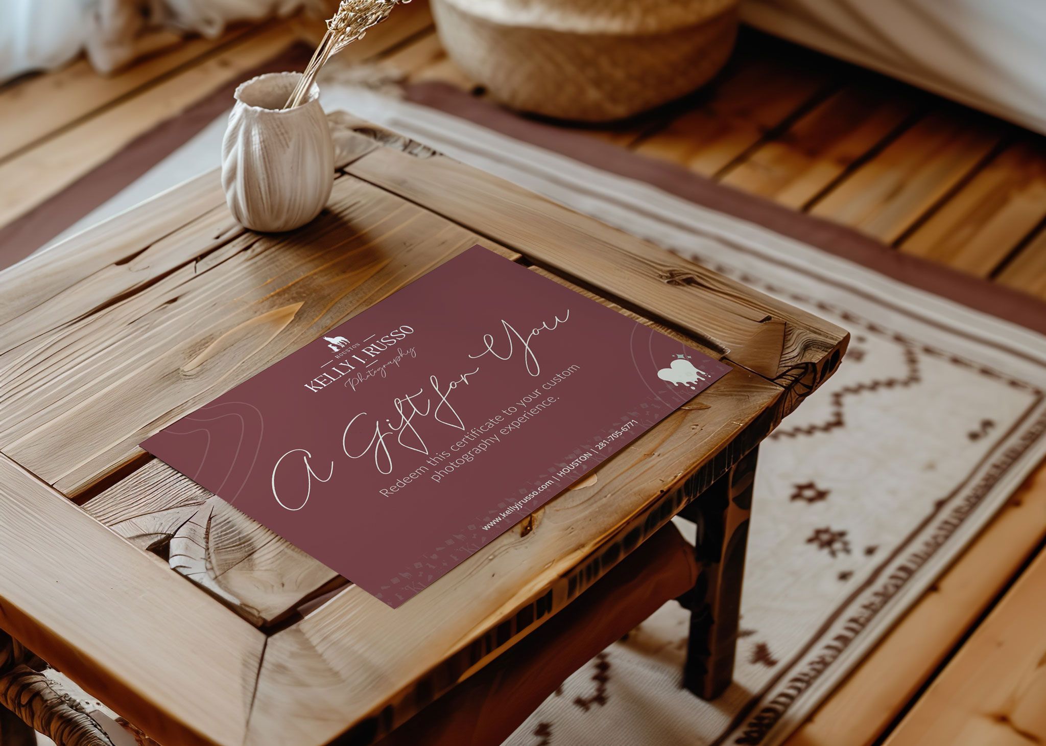 A burgundy photography gift certificate sits on a rustic wooden desk with a glass inkwell and white quill pen.