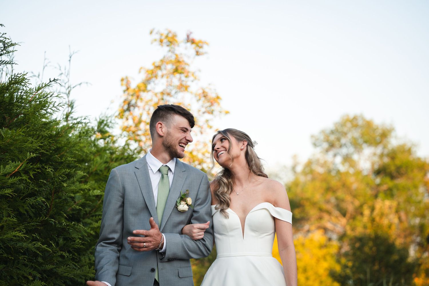 Couple walks together in formal attire through a garden setting with autumn foliage in the background The Barn at Villa Venezia Middletown.