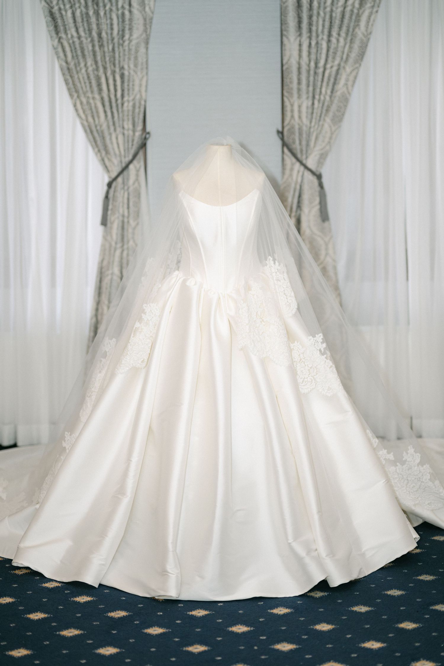 Multiple views of an elegant white satin wedding gown with a full skirt and train displayed on a patterned blue carpet.