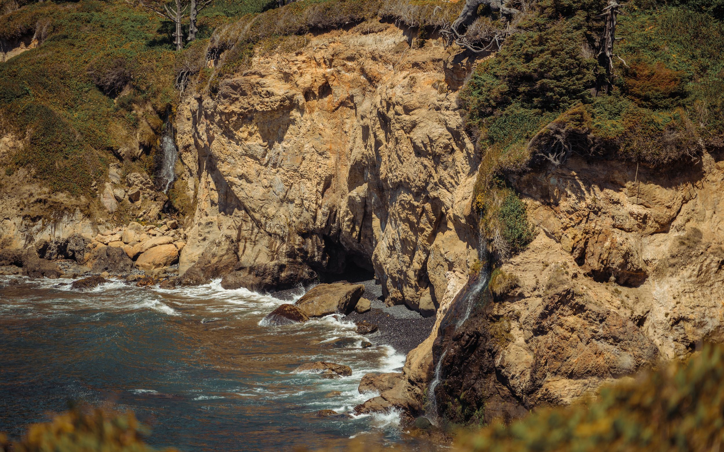 Rugged coastal cliffs meet crashing ocean waves along a dramatic rocky shoreline at sunset.