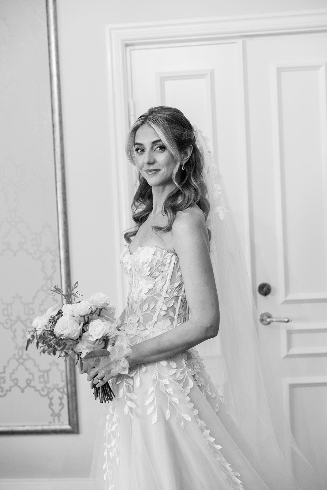 Elegant wedding gowns displayed against a light blue damask wallpaper with gold trim in a luxurious bridal boutique.