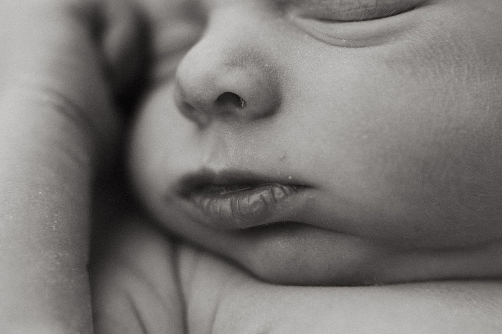 A black and white macro photograph shows soft details of a sleeping baby's nose and lips in gentle light.