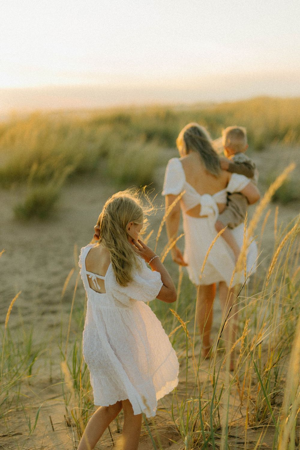 A white-clad figure twirls joyfully among tall beach grass at golden hour, creating a dreamy coastal scene.