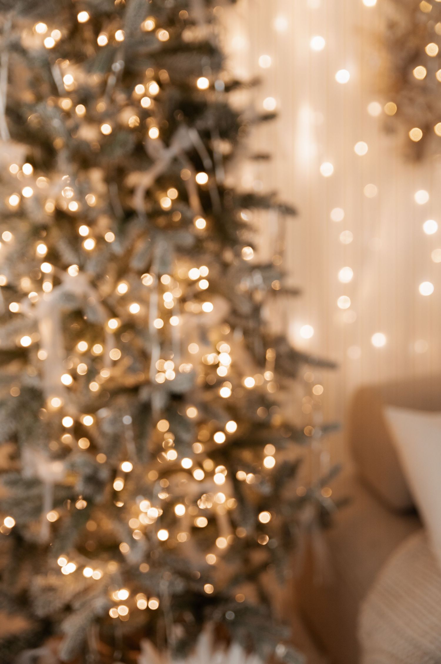 Blurred Christmas tree lights create a magical bokeh effect with warm golden glowing orbs against a soft neutral background.