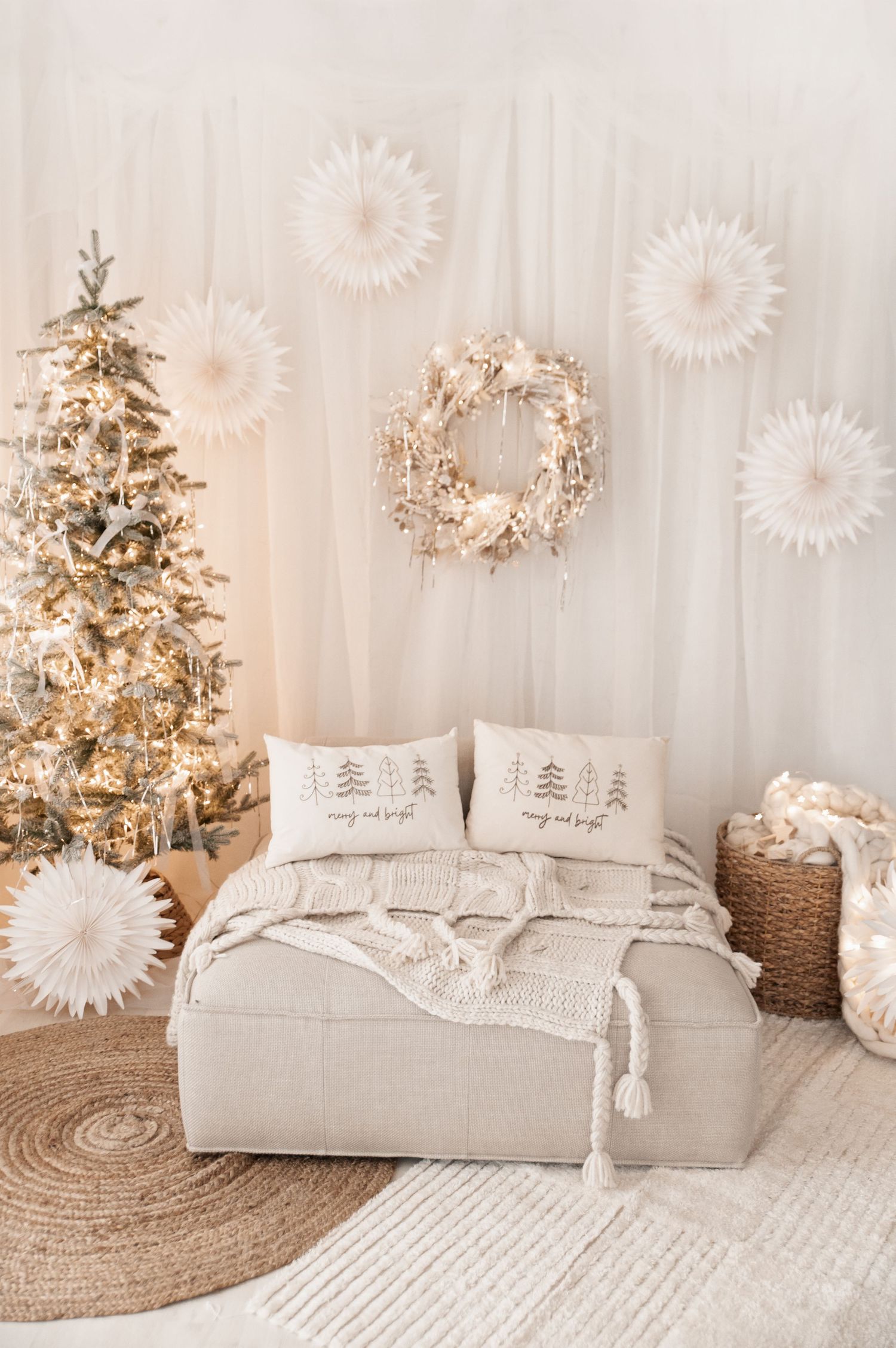 White and gold holiday decor with cozy cushions, Christmas tree, and snowflake wall decorations in a serene living space.