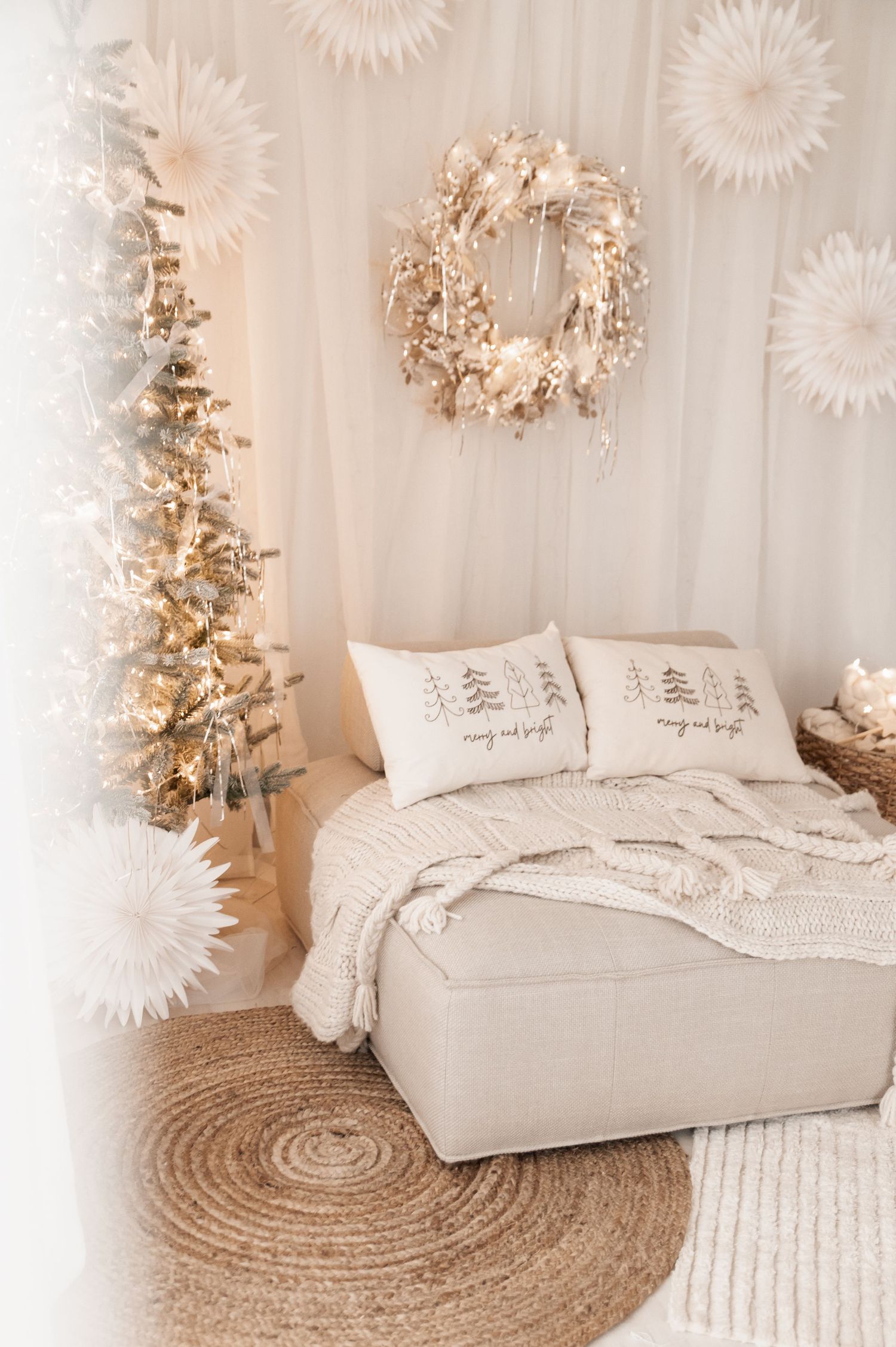 Cozy white bedroom with Christmas tree, jute rug, and white starburst decorations on wall creates serene holiday atmosphere.