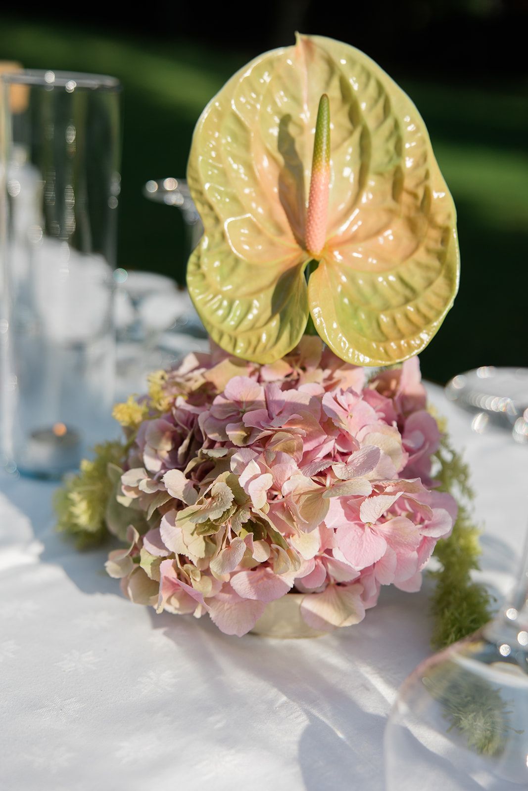 Long wooden banquet tables with place settings arranged outdoors on a lush green lawn beside a rocky outcrop.