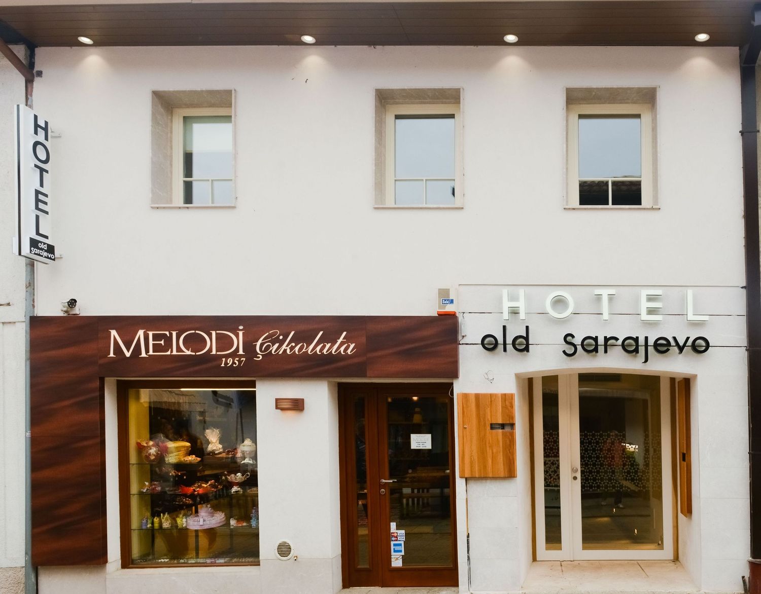 A row of small storefronts with white walls and wooden accents including a chocolate shop called Merodi Chocolate.