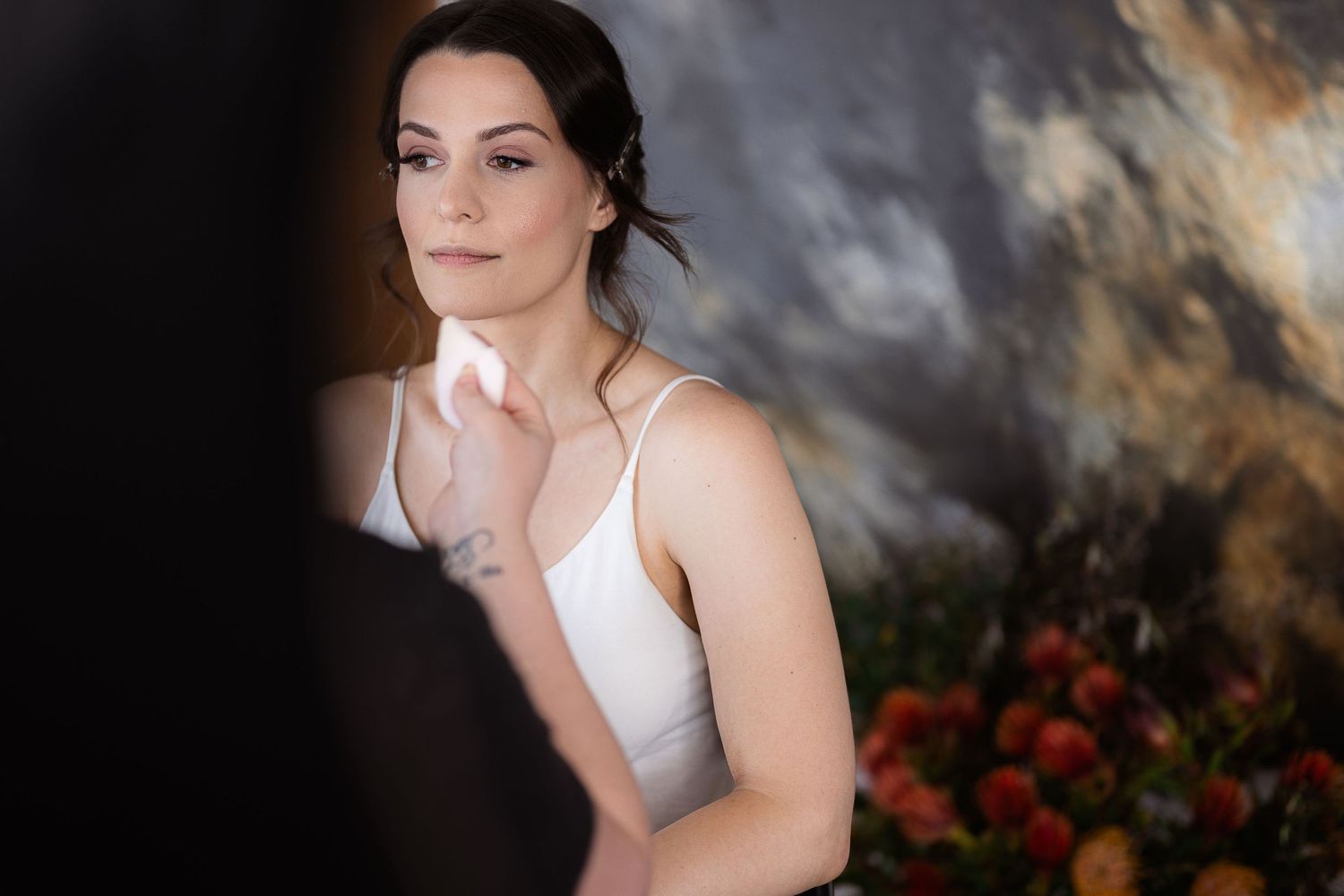 A person in a white dress poses gracefully against a dramatic dark background with red flowers visible.