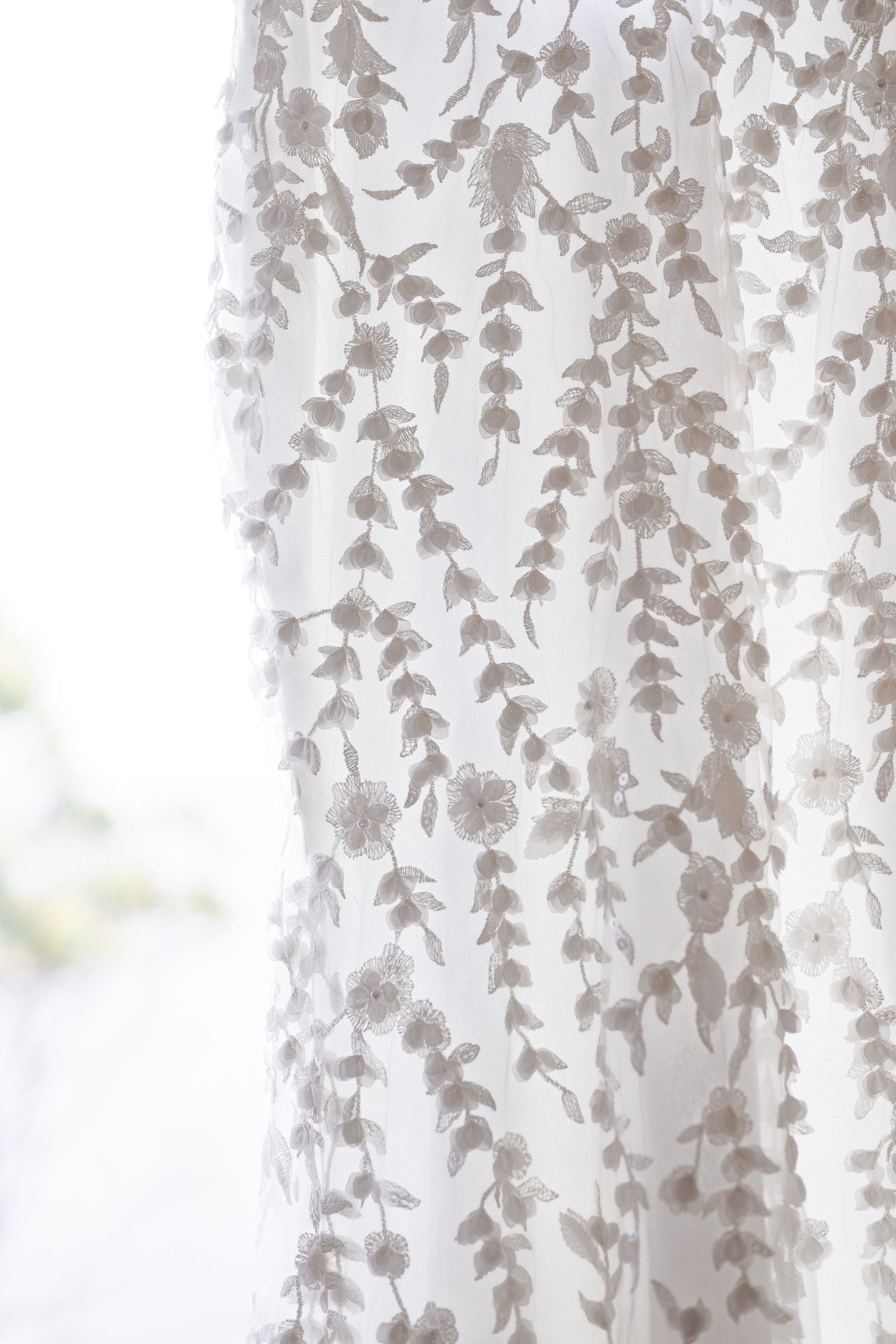 White sheer curtains with delicate leaf pattern design filter soft natural light through a window.