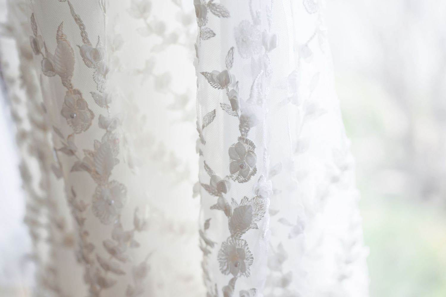 Close-up view of delicate white lace curtain with floral pattern design showing soft light filtering through.