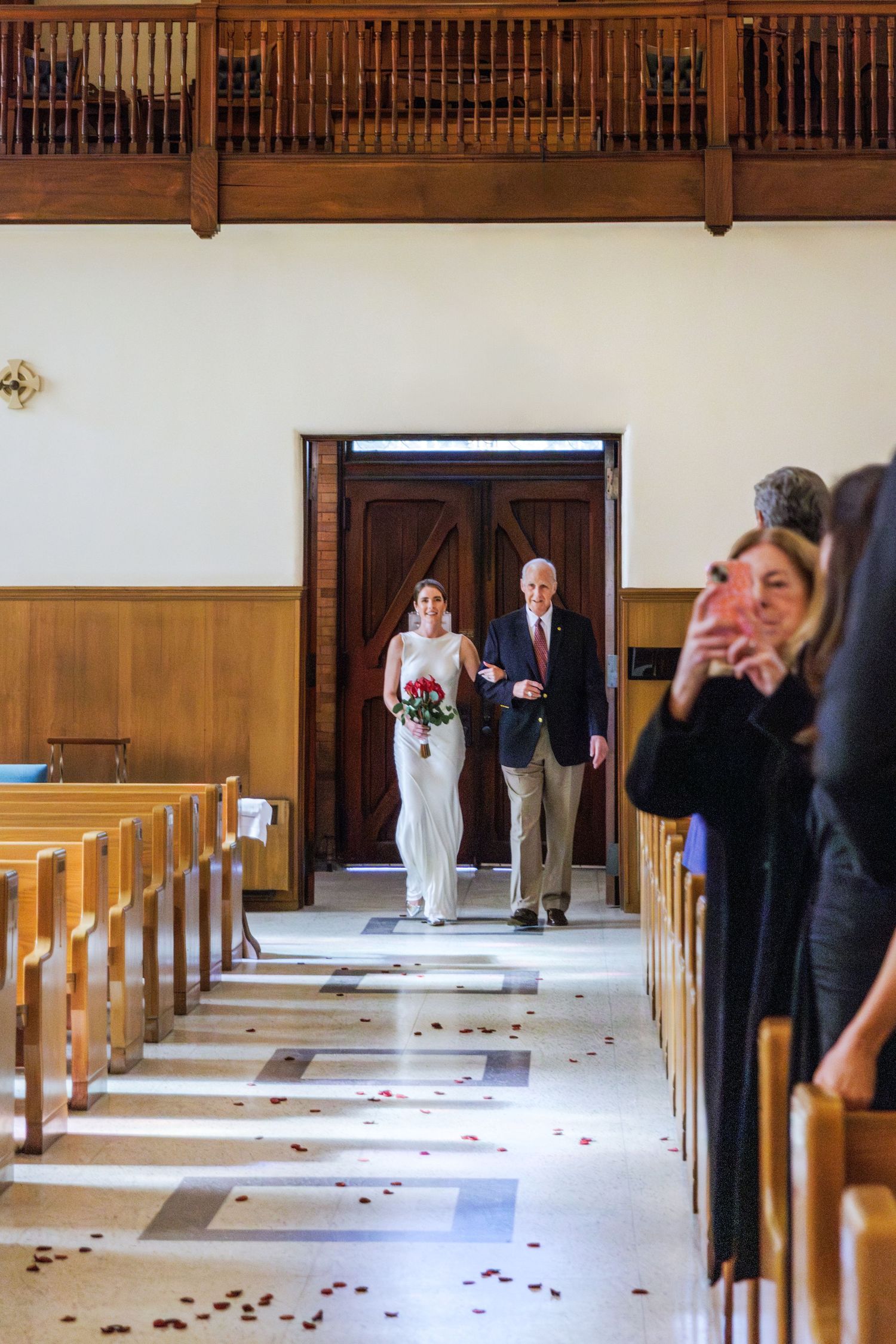 A Bride walking down the aisle in a church decorated with scattered rose petals and wooden pews.