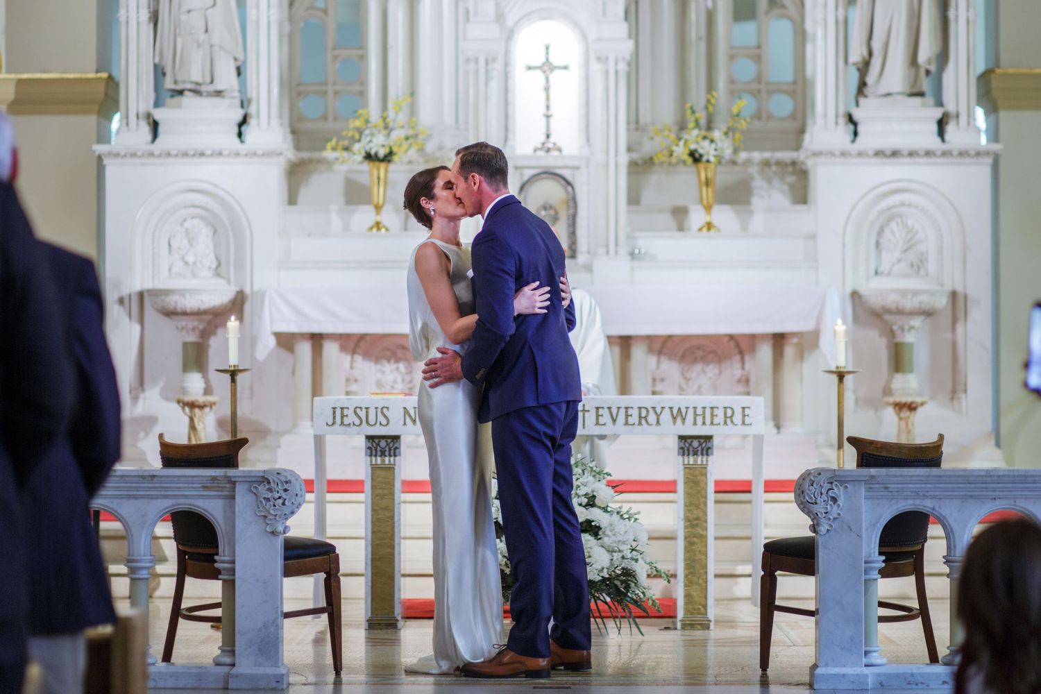 Bride and groom share their first kiss at the front of a white church.