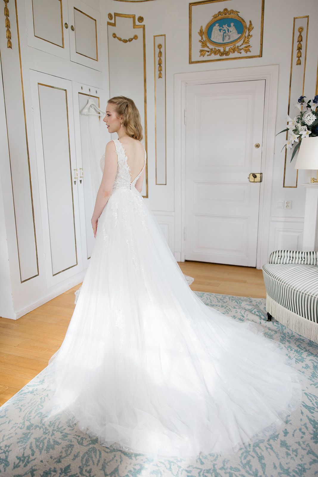 Elegant bride in flowing white wedding gown twirls gracefully on ornate blue and white patterned carpet in luxurious room.