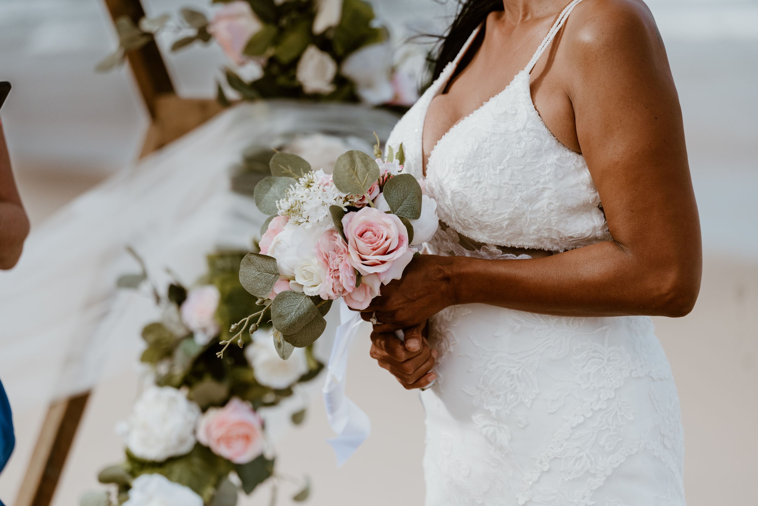 Close up of bridal bouquet with pink roses and white flowers against wedding dress.