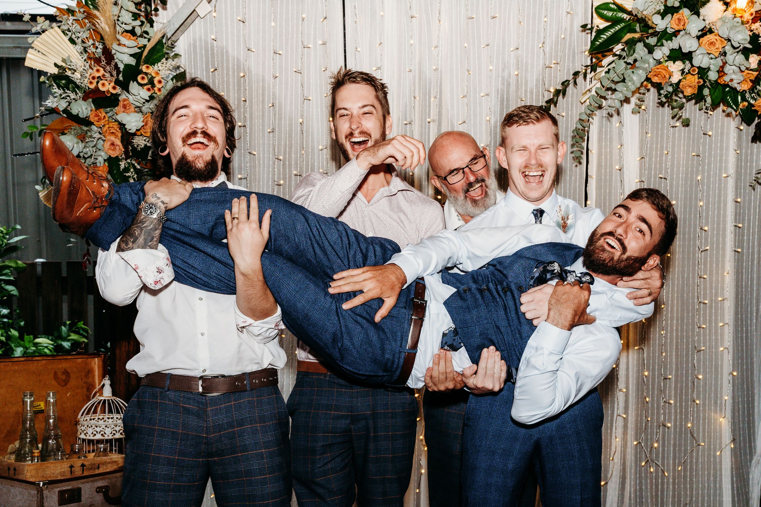 Four groomsmen in suits playfully carry and pose for a fun group photo.