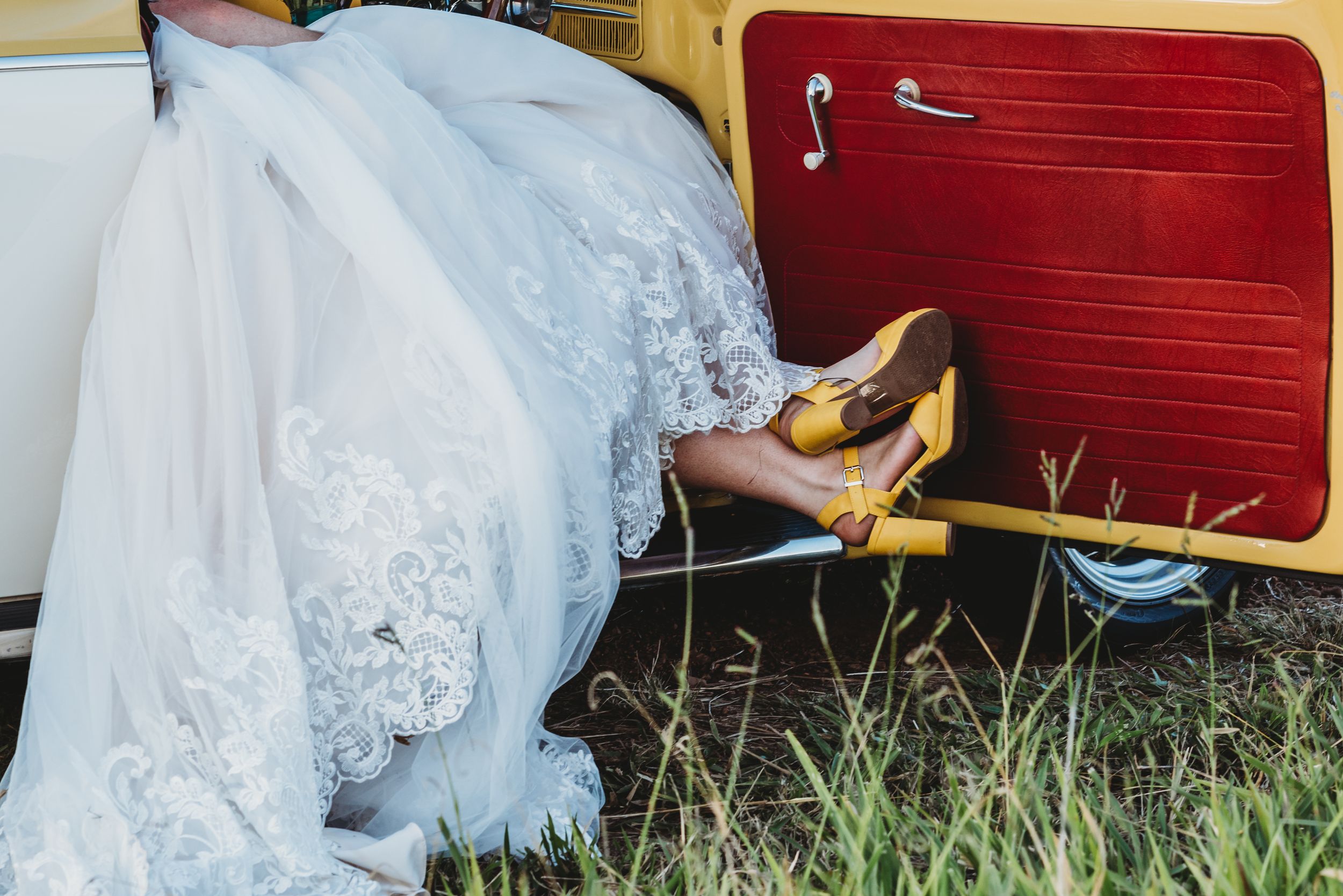 Wedding dress detail with yellow heels against red vintage car door.