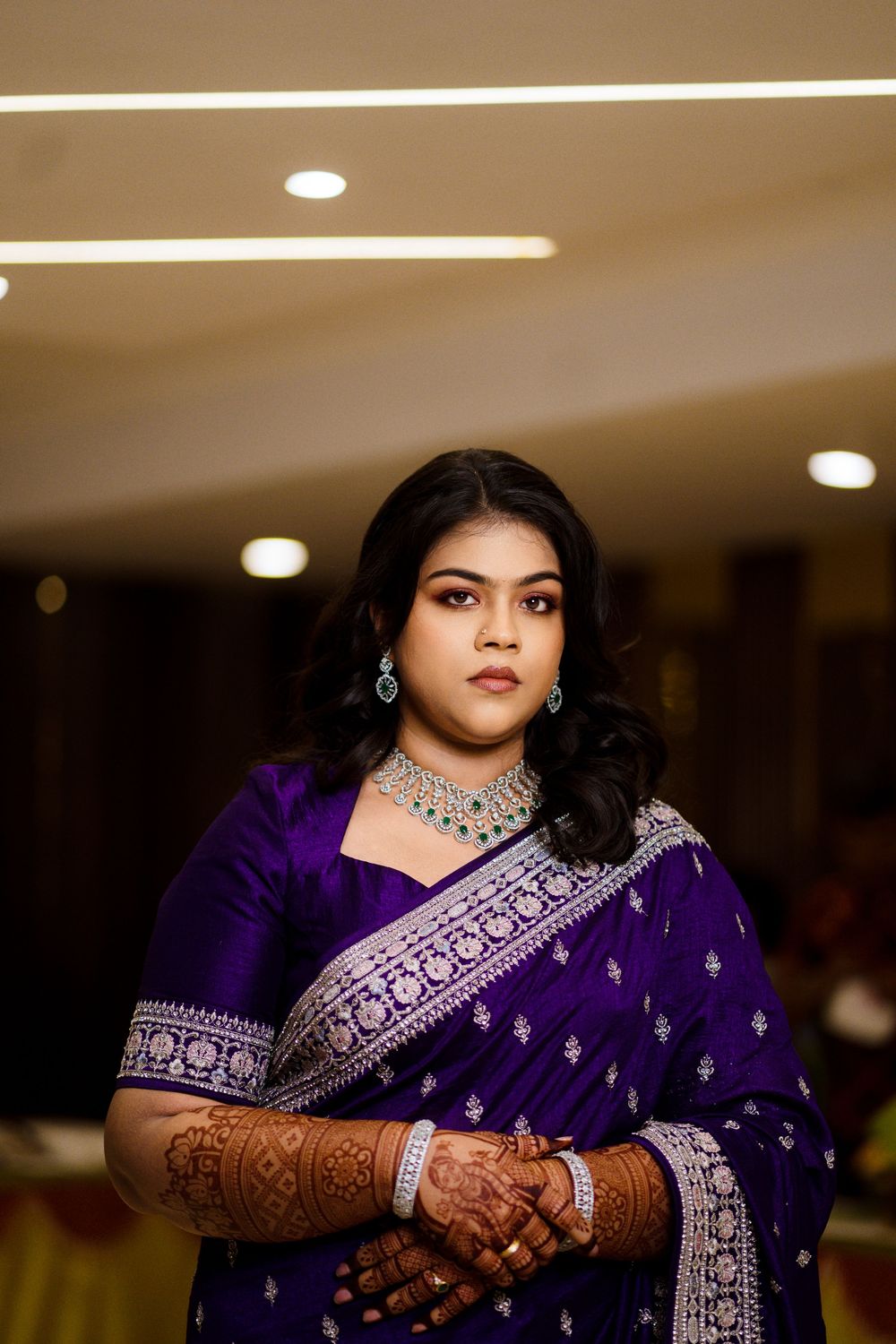 A person wearing a deep purple and silver embroidered sari with intricate henna designs and jewelry.