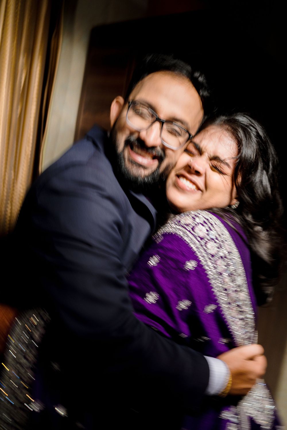 A couple in a tender embrace share joyful laughter while wearing purple and navy outfits.