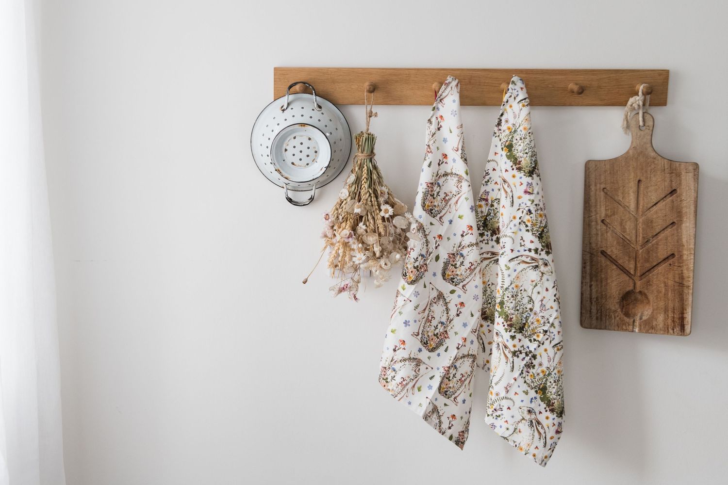 Rustic kitchen items hanging on oak pegs with dried flowers and tea towels and napkins