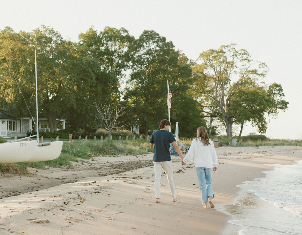 Family walking along a sandy beach path at sunset with trees and coastal vegetation in the background.