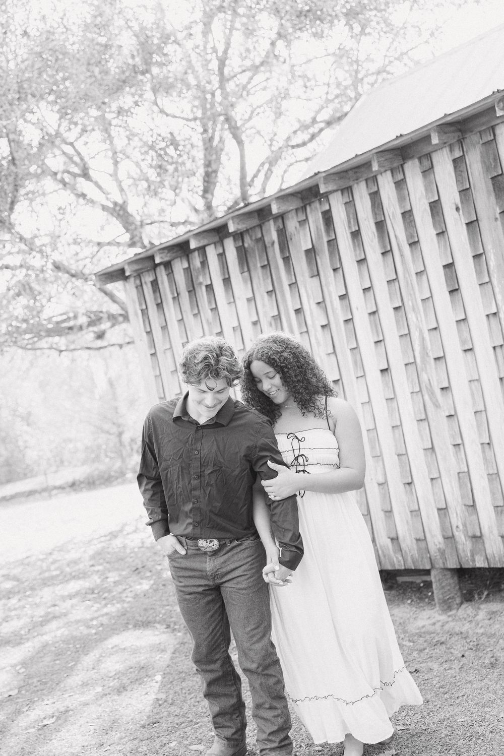 A couple in wedding attire poses together against a white picket fence in a romantic outdoor setting.