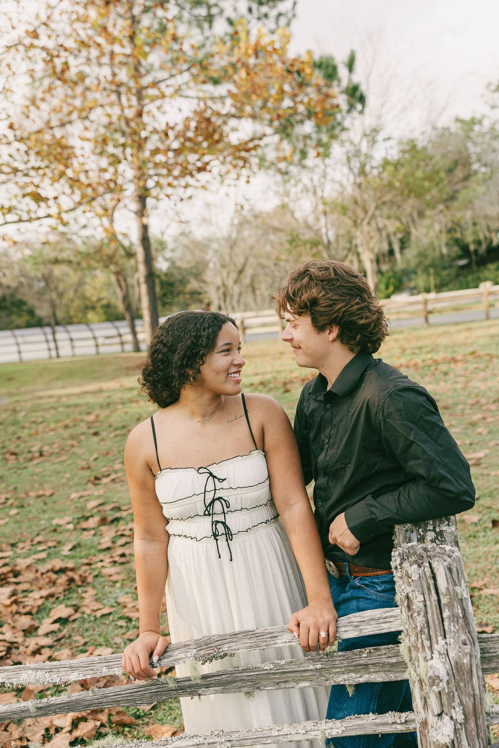 A couple shares a tender moment while sitting on a rustic wooden fence during an autumn afternoon.