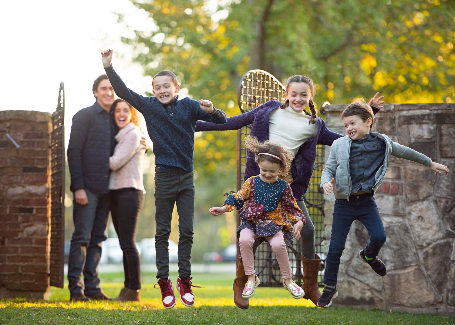 Joyful family with four kids jumping and celebrating outdoors in a lush green park setting.