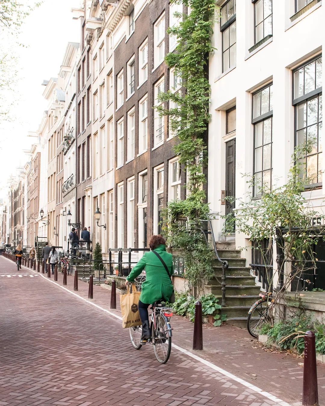 Man riding a bicycle down a quiet brick street in Amsterdam, surrounded by tall narrow houses and greenery.