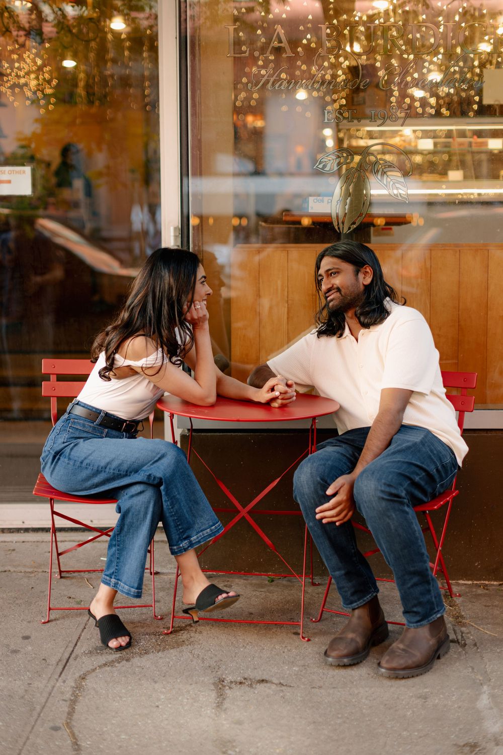 A couple sits together on red outdoor chairs having an intimate conversation at dusk.