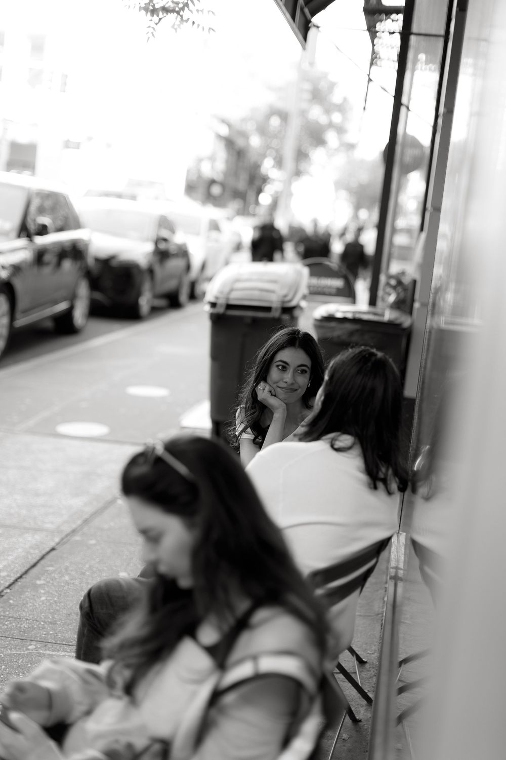 Black and white candid street scene showing people sitting outside a storefront.
