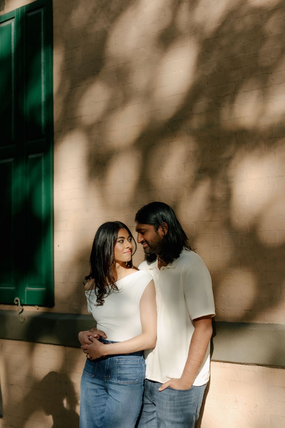 A romantic couple embraces against a sunlit wall with dramatic shadows.