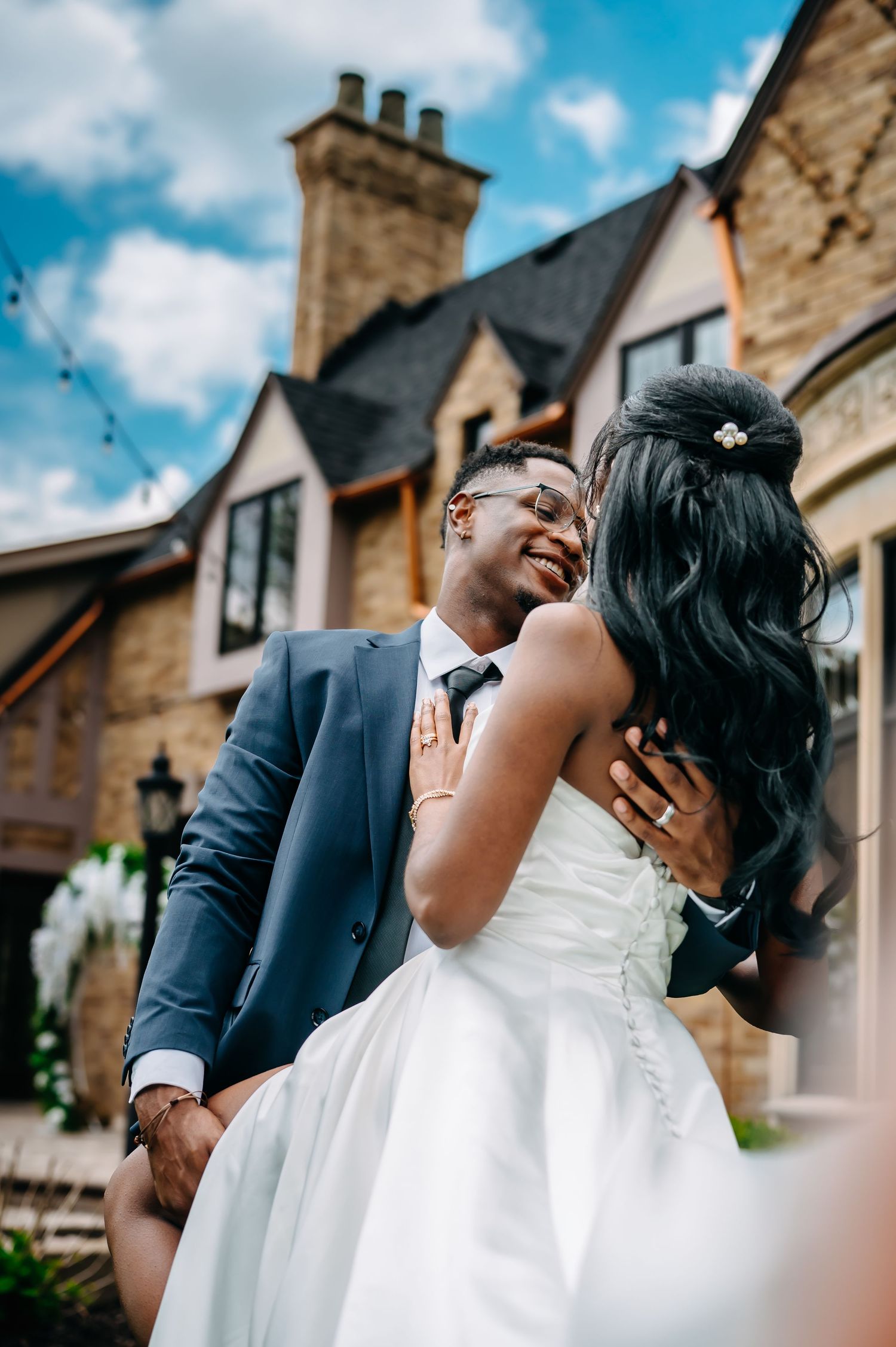 A joyful wedding moment captured outside a stone building with tall chimneys on a cloudy day.