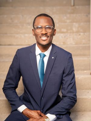 Professional wearing a navy suit and teal tie poses against a beige wall in a series of headshots.