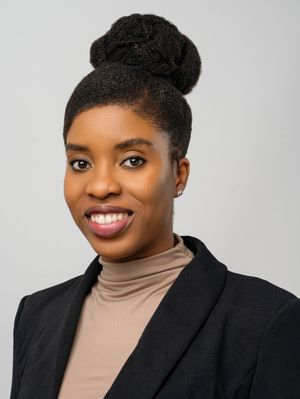 Professional headshot portrait of someone in a black blazer and beige turtleneck against a light background.
