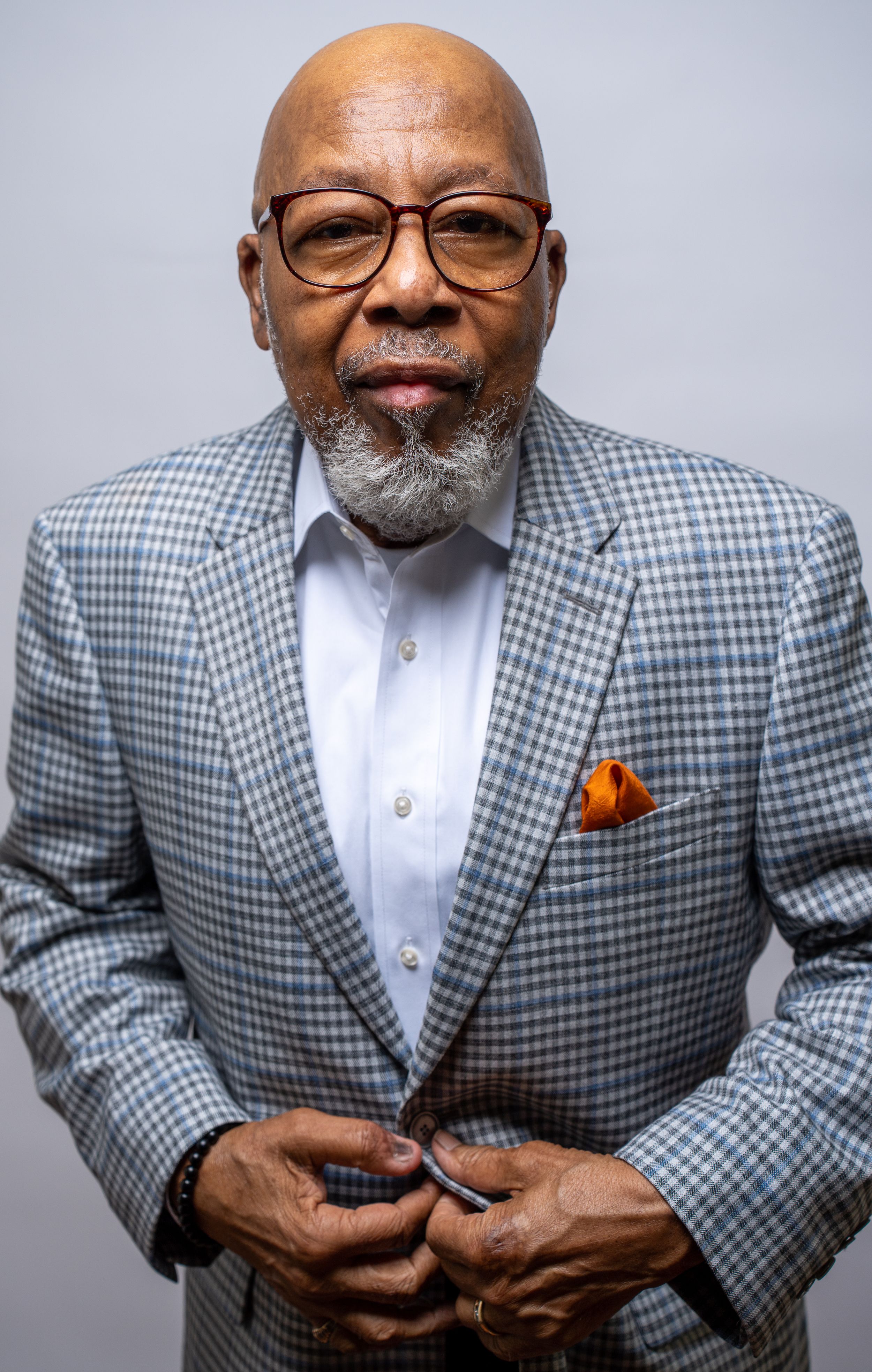 A series of expressive poses in a gray checkered blazer with orange pocket square against a light background.